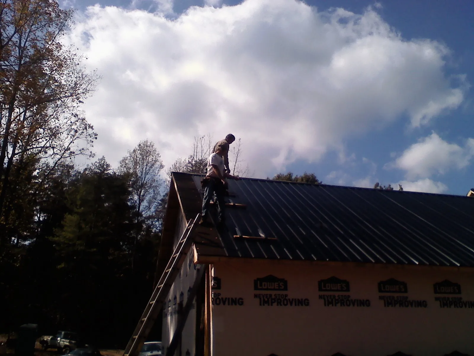 Roofer fastening dark metal panels high against a cloudy sky, from a Roof Inspection job in Oakley
